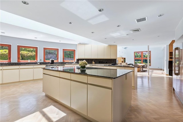 kitchen with a center island, tasteful backsplash, cream cabinets, light parquet floors, and dark stone counters