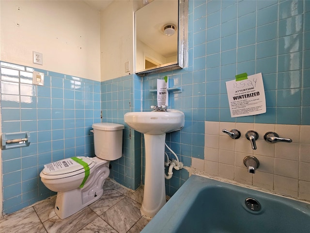 bathroom featuring toilet, a bath, and tile walls