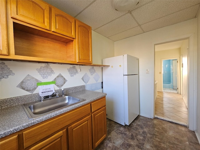 kitchen featuring sink, white refrigerator, a paneled ceiling, and backsplash