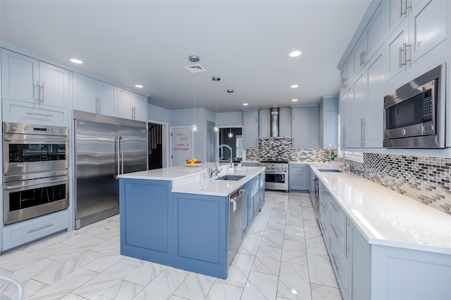 kitchen with pendant lighting, a center island with sink, sink, built in appliances, and wall chimney exhaust hood