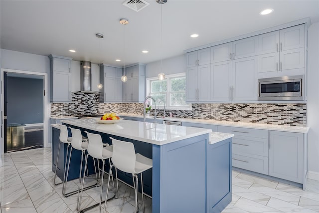 kitchen with a kitchen breakfast bar, hanging light fixtures, wall chimney exhaust hood, a kitchen island, and stainless steel appliances