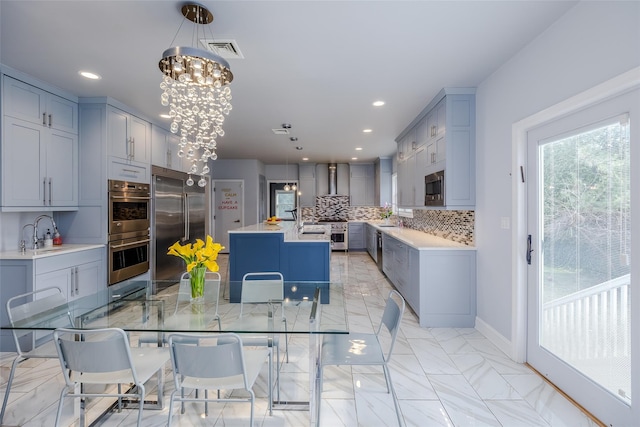 kitchen with pendant lighting, a center island, built in appliances, decorative backsplash, and wall chimney exhaust hood