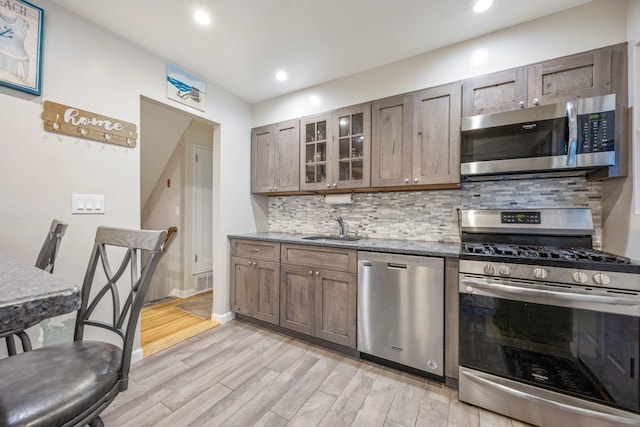 kitchen with decorative backsplash, appliances with stainless steel finishes, dark stone counters, sink, and light hardwood / wood-style flooring