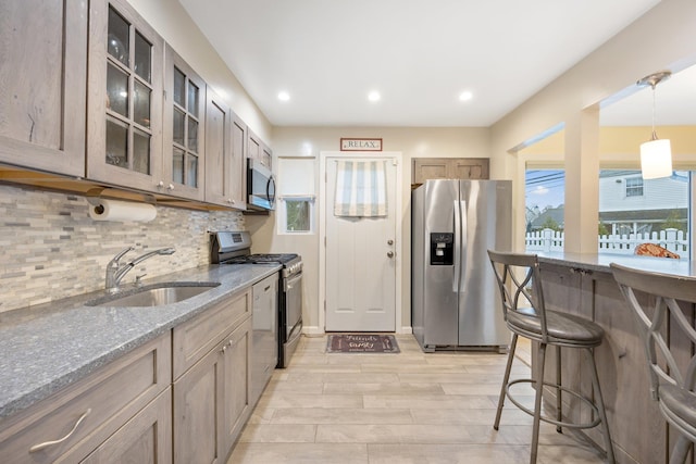 kitchen with light stone countertops, decorative backsplash, stainless steel appliances, sink, and hanging light fixtures