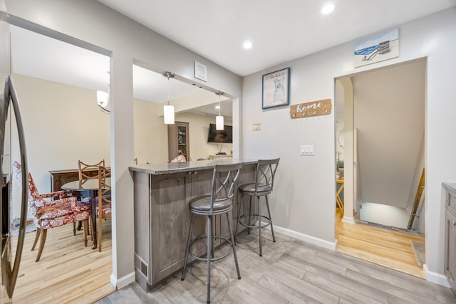 kitchen with kitchen peninsula, a kitchen breakfast bar, light wood-type flooring, light stone countertops, and pendant lighting