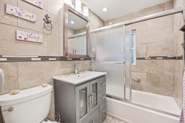 full bathroom with shower / bath combination with glass door, vanity, toilet, and tile walls