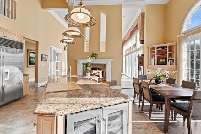 kitchen with light stone countertops, stainless steel built in fridge, beverage cooler, a towering ceiling, and a fireplace