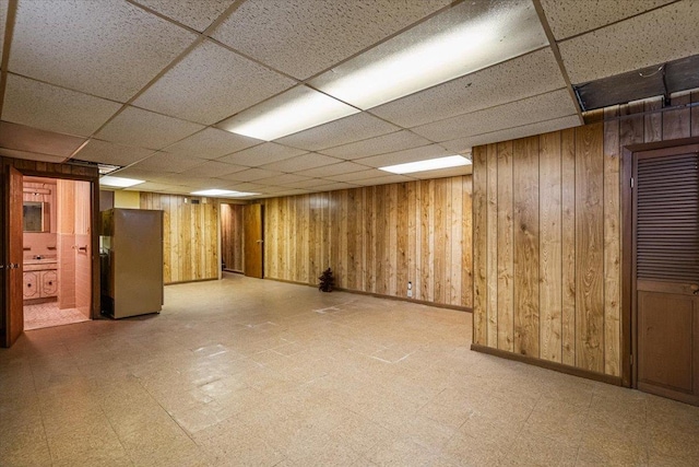 basement featuring stainless steel fridge, a paneled ceiling, and wood walls