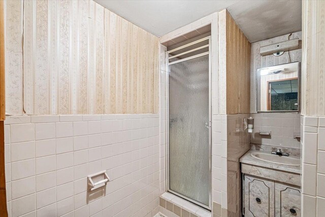 bathroom featuring walk in shower, vanity, and tile walls