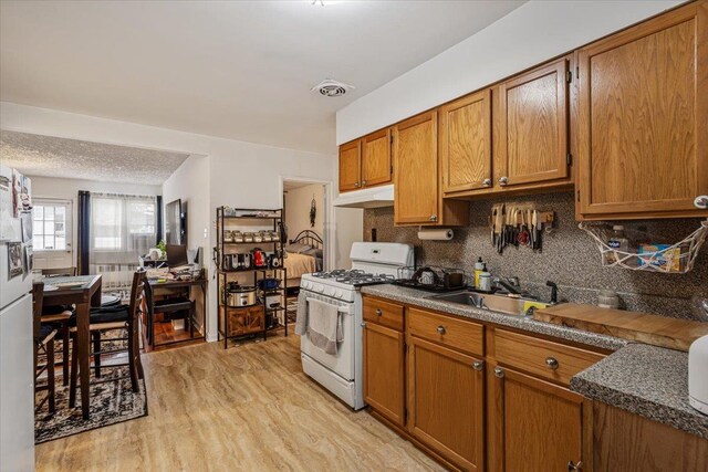 kitchen featuring gas range gas stove, sink, tasteful backsplash, light hardwood / wood-style flooring, and a textured ceiling