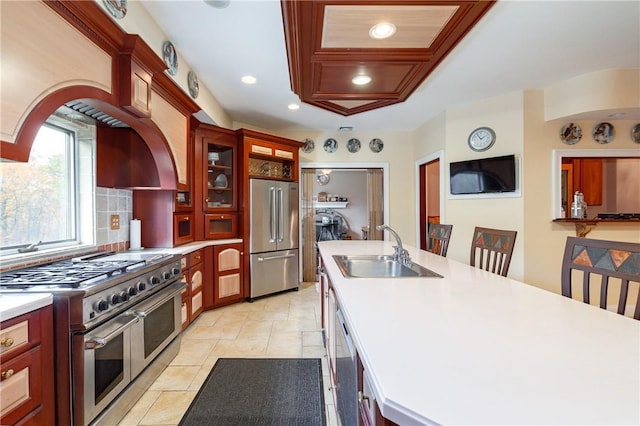 kitchen featuring sink, backsplash, an island with sink, high quality appliances, and light tile patterned floors