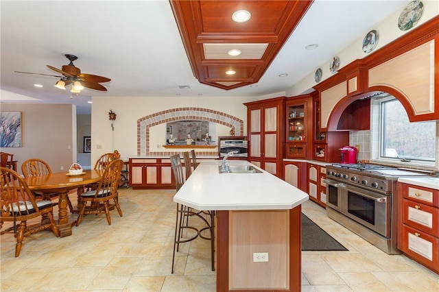 kitchen featuring a breakfast bar, a center island with sink, sink, ceiling fan, and appliances with stainless steel finishes