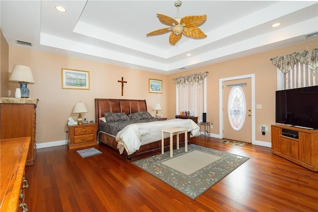 bedroom with dark hardwood / wood-style floors, ceiling fan, and a tray ceiling