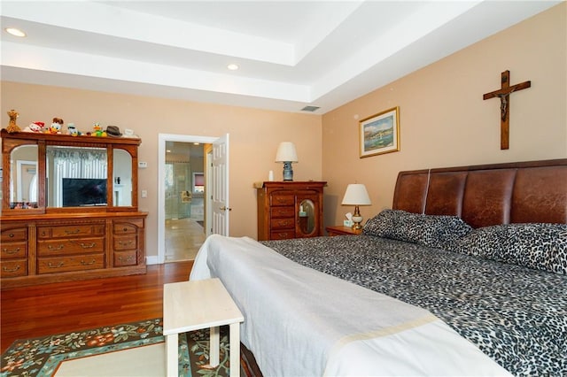 bedroom featuring a raised ceiling, hardwood / wood-style flooring, and ensuite bath