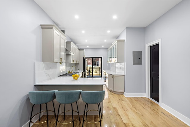 kitchen with gray cabinetry, electric panel, a kitchen breakfast bar, light hardwood / wood-style floors, and kitchen peninsula