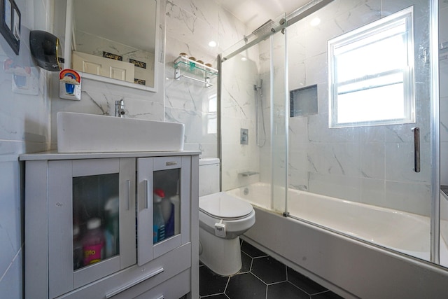 full bathroom with combined bath / shower with glass door, tile patterned floors, toilet, vanity, and tile walls