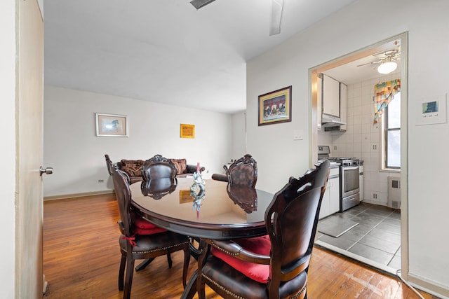 dining room featuring ceiling fan, radiator heating unit, wood-type flooring, and tile walls