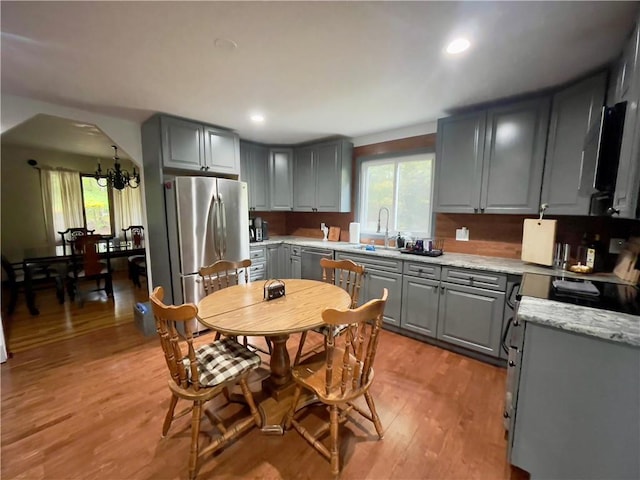 kitchen with appliances with stainless steel finishes, light hardwood / wood-style floors, gray cabinetry, and a notable chandelier