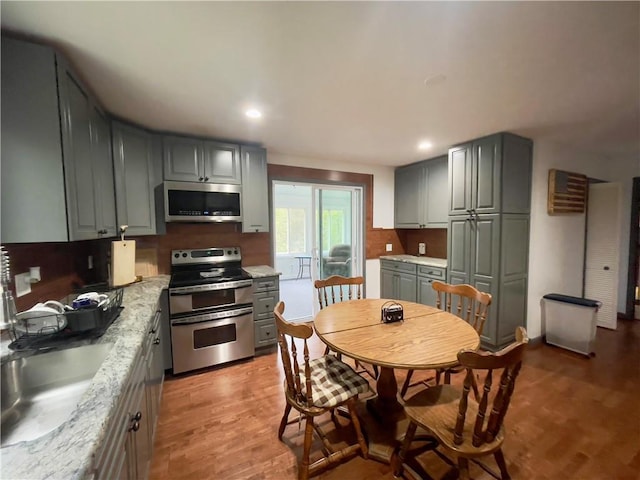 kitchen featuring sink, gray cabinets, light wood-type flooring, light stone counters, and stainless steel appliances