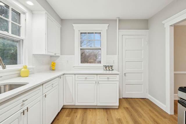 kitchen featuring decorative backsplash, white cabinetry, sink, and light hardwood / wood-style flooring