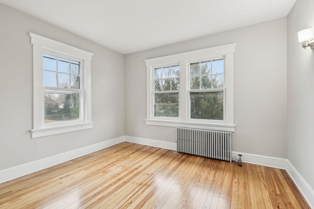 spare room with hardwood / wood-style floors, radiator, and a healthy amount of sunlight