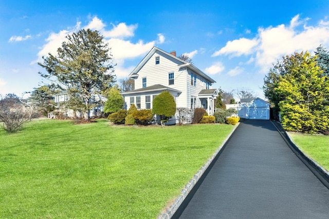 view of side of home with an outbuilding, aphalt driveway, a detached garage, a yard, and a chimney