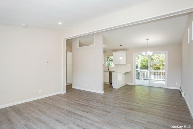 unfurnished living room with light hardwood / wood-style flooring, a baseboard radiator, and an inviting chandelier