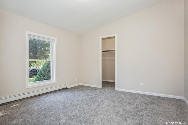 unfurnished bedroom with vaulted ceiling, baseboard heating, a spacious closet, carpet floors, and a closet