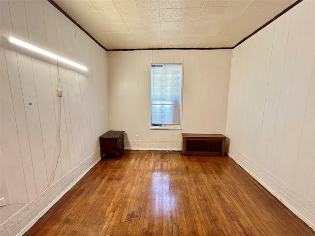 empty room featuring hardwood / wood-style flooring, crown molding, radiator, and wooden walls