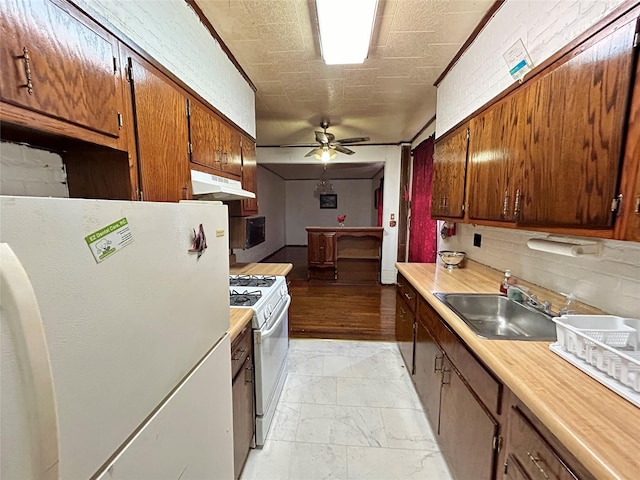 kitchen with brick wall, white appliances, ceiling fan, sink, and light hardwood / wood-style flooring