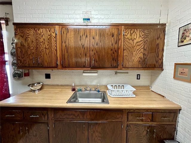 kitchen featuring backsplash, sink, and brick wall