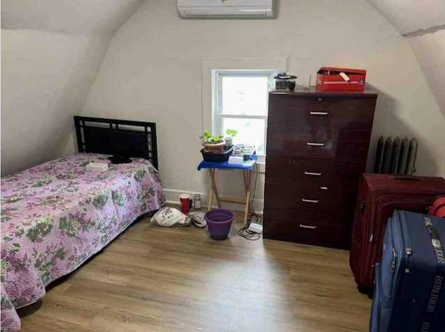 bedroom with vaulted ceiling, light wood-type flooring, and a wall mounted AC