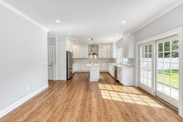 kitchen featuring plenty of natural light, white cabinets, wall chimney range hood, and appliances with stainless steel finishes