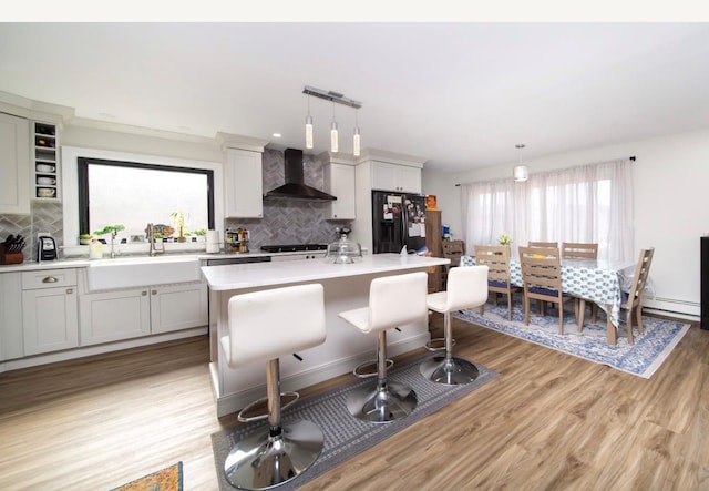 kitchen with a center island, wall chimney exhaust hood, black refrigerator with ice dispenser, backsplash, and decorative light fixtures