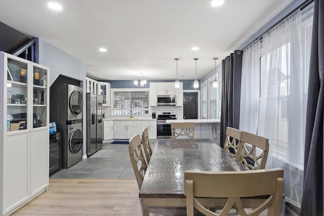 dining area featuring a notable chandelier, light wood-type flooring, sink, and stacked washer and clothes dryer