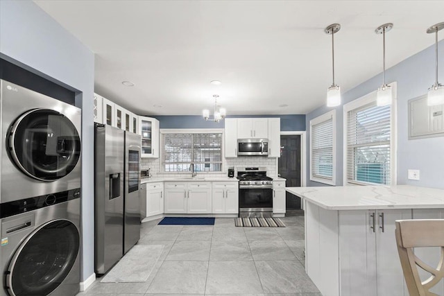 kitchen featuring kitchen peninsula, appliances with stainless steel finishes, pendant lighting, white cabinetry, and stacked washer / drying machine