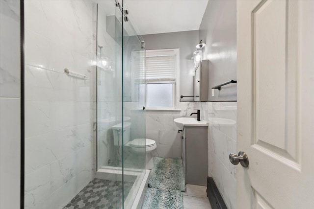 bathroom with tile patterned floors, vanity, a shower with door, tile walls, and toilet