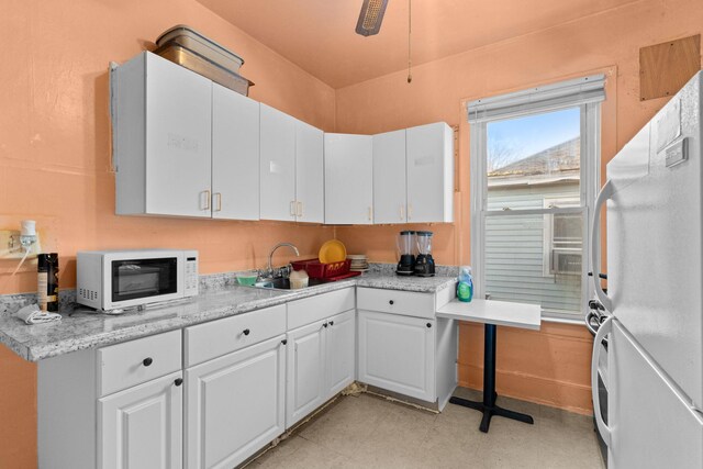 kitchen featuring light stone counters, white appliances, ceiling fan, sink, and white cabinetry