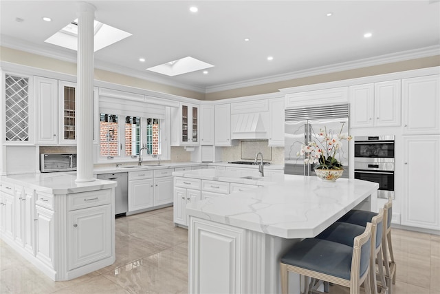 kitchen with a center island with sink, white cabinets, sink, light stone counters, and stainless steel appliances