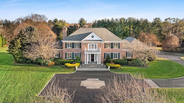 colonial inspired home featuring a balcony and a front yard