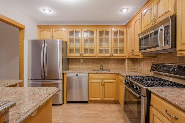 kitchen featuring sink, backsplash, stainless steel appliances, light stone countertops, and light hardwood / wood-style flooring