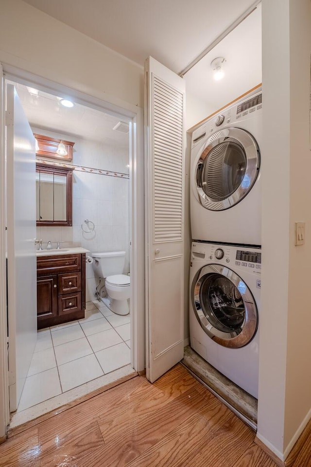 laundry room featuring stacked washer and dryer, sink, tile walls, and light tile patterned floors