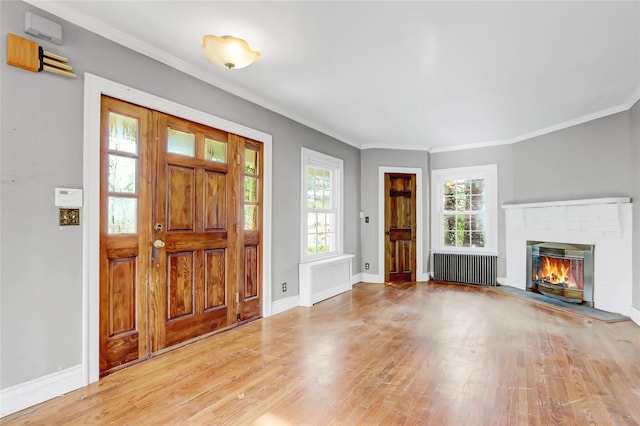 foyer entrance with light wood-type flooring, radiator heating unit, ornamental molding, and a brick fireplace