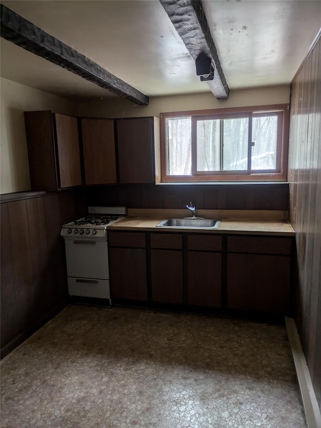 kitchen with wood walls, dark brown cabinetry, gas range gas stove, and sink