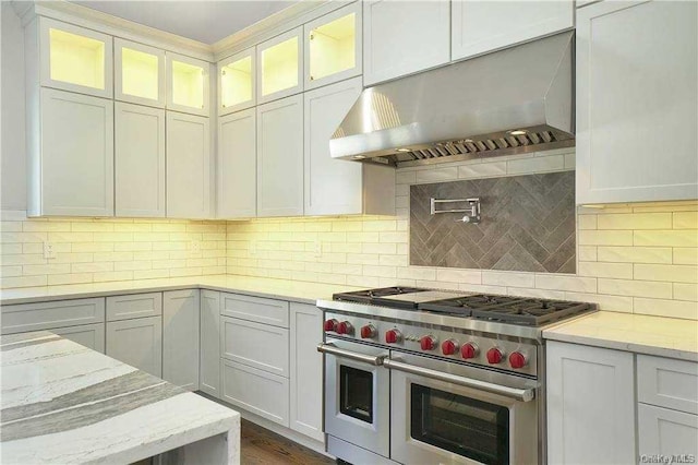 kitchen with under cabinet range hood, double oven range, tasteful backsplash, and glass insert cabinets