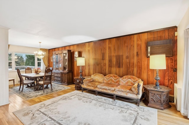 living room featuring ornamental molding, light wood-type flooring, wooden walls, and a notable chandelier