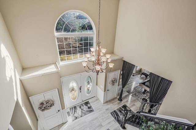 foyer entrance with a towering ceiling, a notable chandelier, and light wood-type flooring