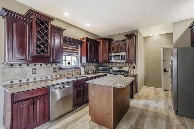 kitchen with light wood-type flooring, backsplash, stainless steel appliances, sink, and a center island