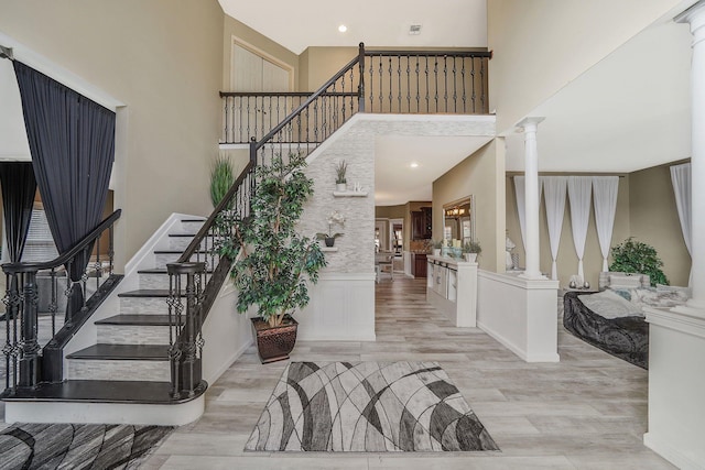 entrance foyer with a towering ceiling, light wood-type flooring, and decorative columns