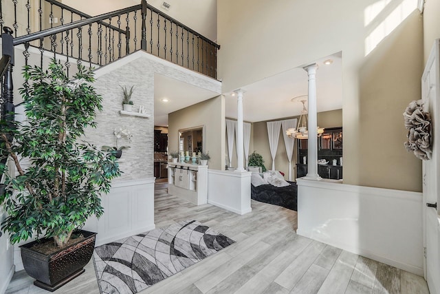 foyer featuring ornate columns, a notable chandelier, a high ceiling, and light wood-type flooring